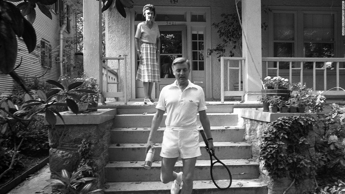 Mondale heads out to play tennis while his wife Joan stands on the porch of their Washington, DC, home in 1983.