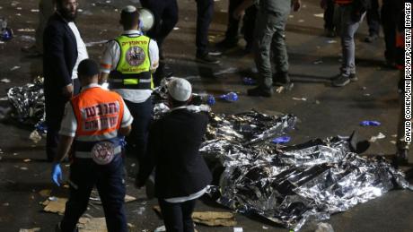 TOPSHOT - Paramedics and ultra-Orthodox Jewish men stand next to covered bodies after dozens of people were killed and others injured after a grandstand collapsed in Meron, Israel, where tens of thousands of people were gathered to celebrate the festival of Lag Ba&#39;omer at the site in northern Israel early on April 30, 2021. - Dozens of people were killed in a stampede at a Jewish pilgrimage site in the north of Israel on early on April 30, rescue services said.  Tens of thousands of Jews were participating in the annual pilgrimage on Thursday, for the feast of Lag BaOmer. But after midnight, a grandstand collapsed, triggering scenes of panic. - Israel OUT (Photo by David COHEN / JINI PIX / AFP) / Israel OUT (Photo by DAVID COHEN/JINI PIX/AFP via Getty Images)