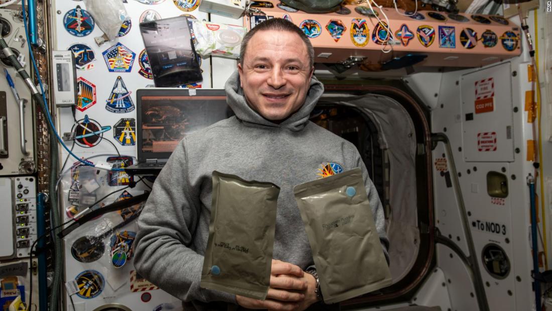 NASA astronaut and Expedition 61 Flight Engineer Andrew Morgan poses with two food packets, chicken with cornbread and chocolate pudding, during dinnertime aboard the International Space Station&#39;s Unity module, January 1, 2019.