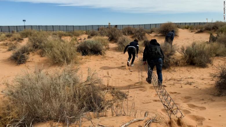 A smuggler leads two migrants toward the wall on the US-Mexico border in Ciudad Juárez, Mexico, dragging the makeshift ladder.