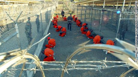 Detainees wearing orange jumpsuits are seen under guard on January 11, 2002 in a holding area at Camp X-Ray, on the US Naval Base at Guantanamo Bay, Cuba.