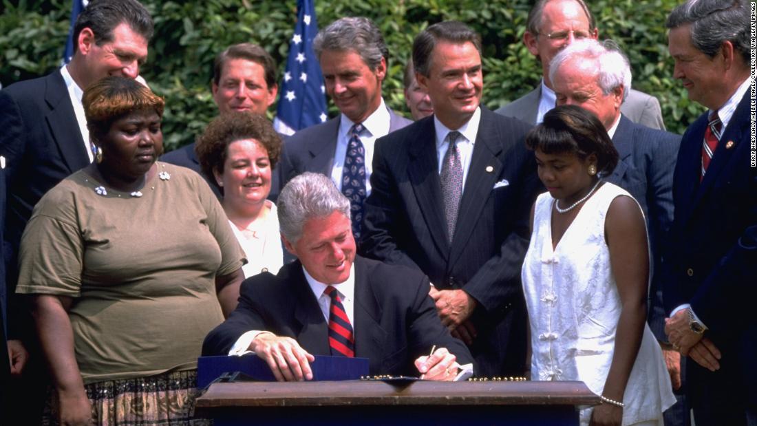 President Bill Clinton signs a controversial welfare reform bill in the White House Rose Garden in 1996 as former welfare recipients and others look on.