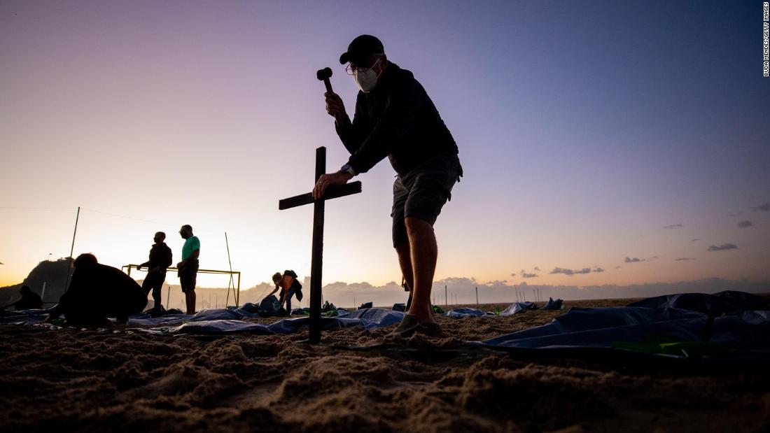 A member of the group Rio de la Paz places a cross at Rio de Janeiro&#39;s Copacabana Beach on April 30. It was in preparation for an event marking Brazil&#39;s Covid-19 death toll, which had reached 400,000.