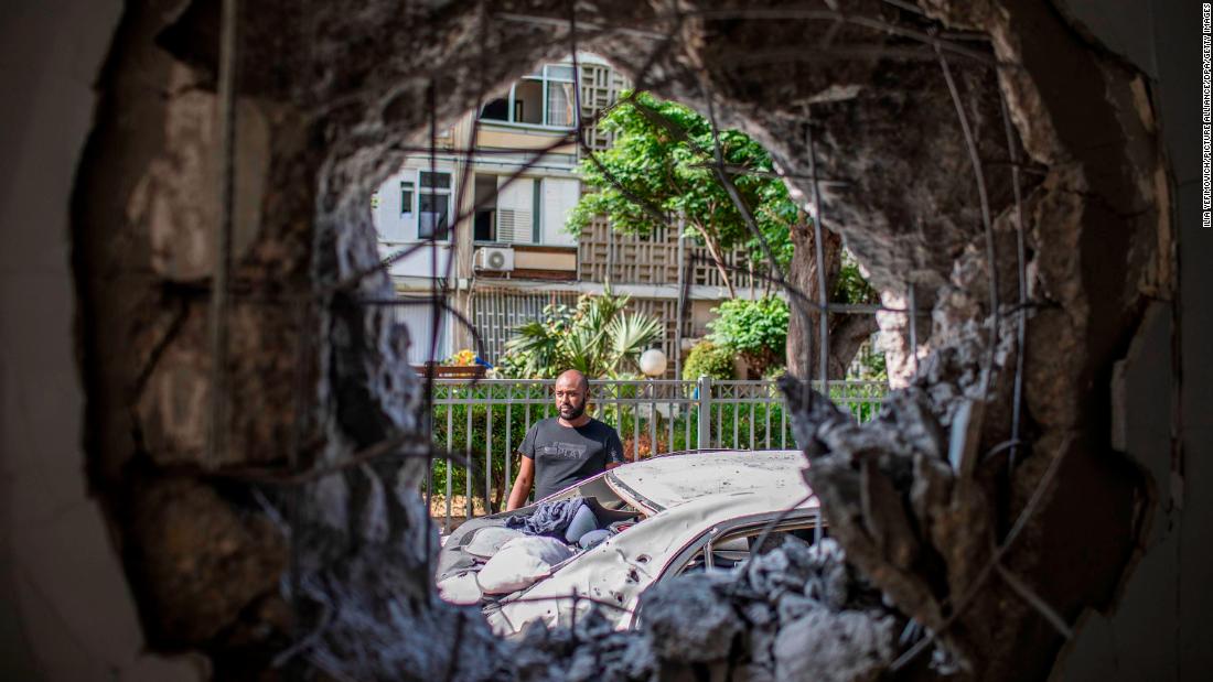 A man in Ashkelon, Israel, views a damaged car and building that was hit by a rocket fired from Gaza.