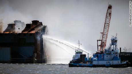 Firefighters working off two tug boats hose down the remains of the overturned cargo ship.