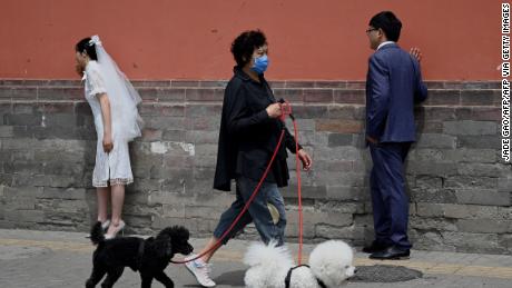 A woman walks her dogs past a couple posing for wedding photographs in Beijing on May 16, 2021.