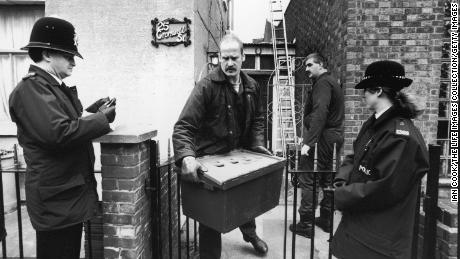 A police investigator walks past a pair of uniformed officers as he carries a large plastic box of evidence from the home of Fred and Rose West at 25 Cromwell Street, Gloucester, England, March 4, 1994.