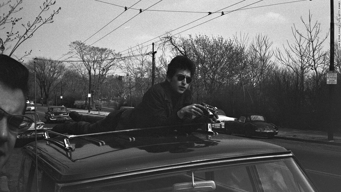 Dylan holds a camera on the top of a car in Massachusetts in 1964.