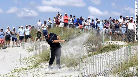 Lowry hits his second shot to the 16th hole from the beach after his tee shot went right and into the dunes.
