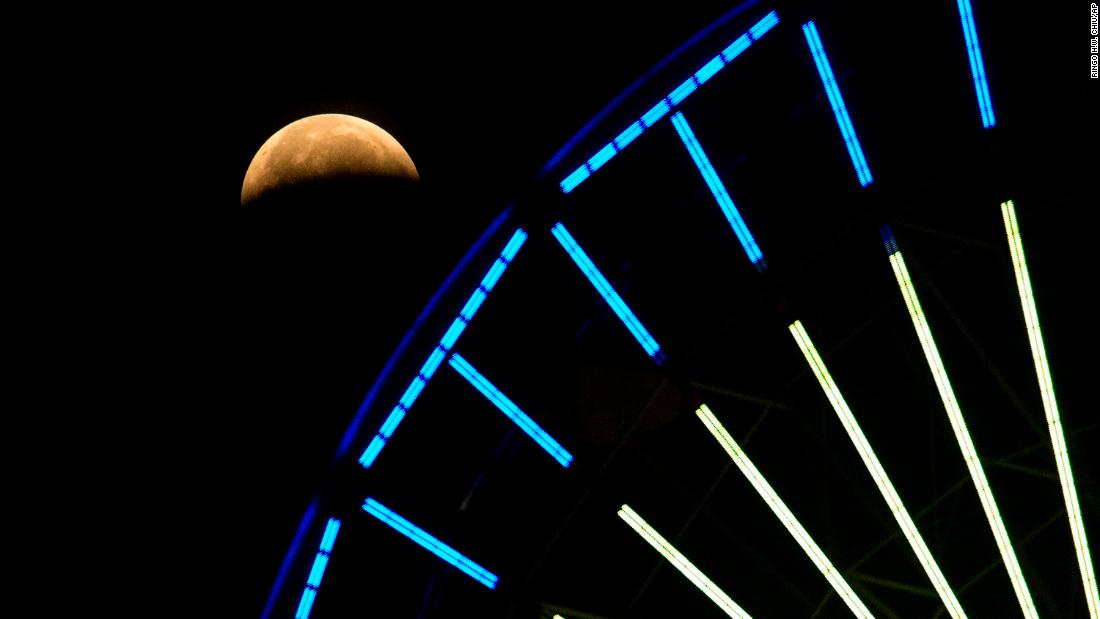 The lunar eclipse is seen behind a Ferris wheel in Santa Monica, California.