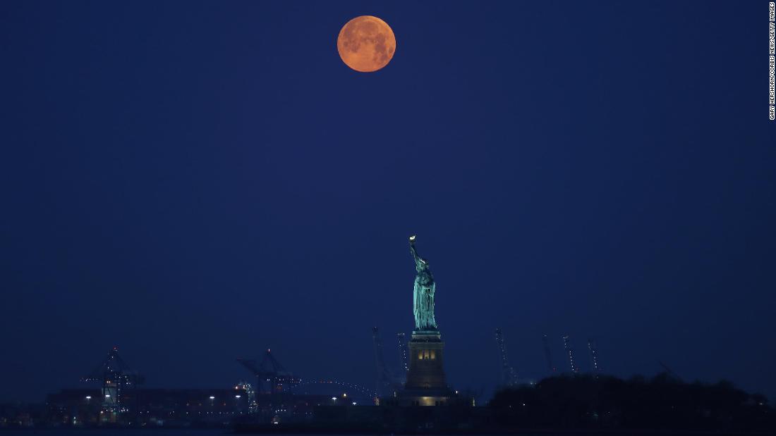 The moon sets behind the Statue of Liberty before sunrise in New York.