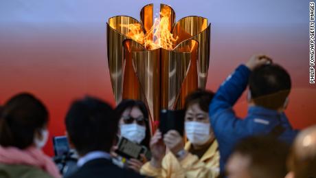 TOPSHOT - People wearing face masks take pictures in front of the Tokyo 2020 Olympic flame, which is displayed outside Sendai railway station, Miyagi prefecture on March 21, 2020, after arriving from Greece. (Photo by Philip FONG / AFP) (Photo by PHILIP FONG/AFP via Getty Images)