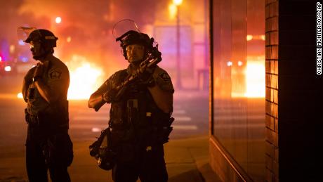 Police stand guard eraly Saturday after protesters set fire to trash bins in Minneapolis.