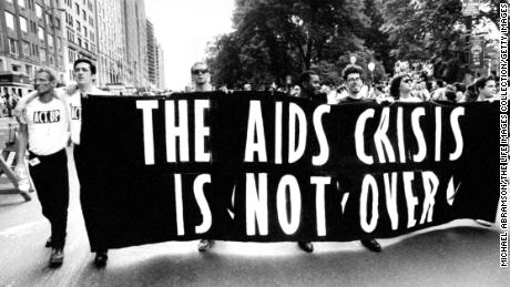 Gay ACT UP members carrying huge banner that reads THE AIDS CRISIS IS NOT OVER as they walk down the street during Gay &amp; Lesbian Pride march. 