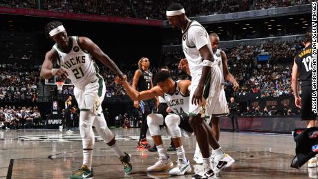 Jrue Holiday and Bobby Portis of the Bucks help up Antetokounmpo during their game against the Nets.