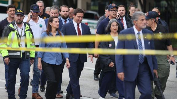 Florida Gov. Ron DeSantis, at center in the red tie, arrives to speak to the media on Thursday. "We still have hope to be able to identify additional survivors," DeSantis told reporters near the scene. "The state of Florida, we're offering any assistance that we can."