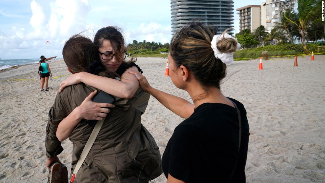 Faydah Bushnaq, center, is hugged by Maria Fernanda Martinez as they stand on the beach near the building. Bushnaq, who was vacationing in South Florida, stopped to write &quot;pray for their souls&quot; in the sand.