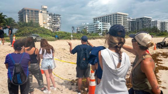 People observe the building from the nearby beach.