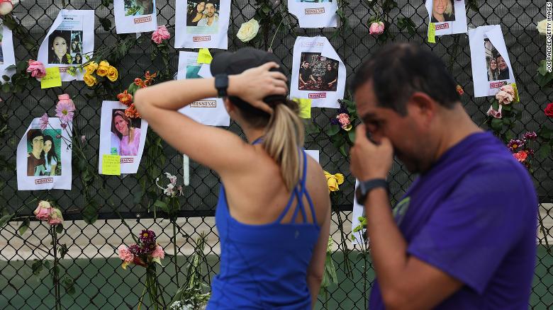 Passersby look at photos of missing people posted to a fence on June 26, 2021, in Surfside, Florida.