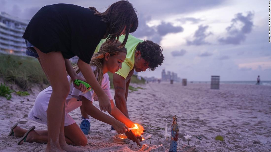 Mourners light candles on the beach near the building.