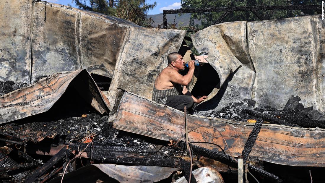 Carlos Torres drinks water on Saturday as he looks for paperwork in his destroyed mobile home in Kelseyville, California. A wind-whipped brush fire burned three mobile homes, two separate garages and vehicles, a single-family dwelling and outbuildings.