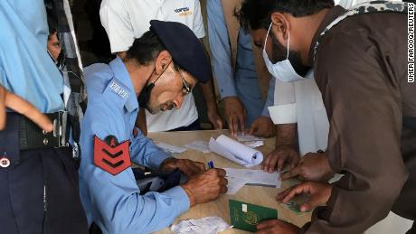 A police officer helps men to fill out forms to obtain a coronavirus vaccine, so they can travel to work abroad, at a mass vaccination centre in Islamabad, Pakistan on June 28, 2021. 