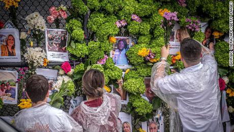 People add flowers to a memorial featuring photos of some of those lost in the partially collapsed 12-story Champlain Towers South building on June 28, 2021 in Surfside.