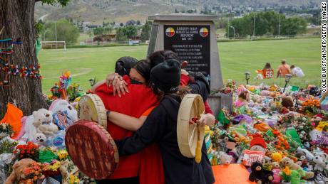 People from Mosakahiken Cree Nation hug in front of a makeshift memorial at the former Kamloops Indian Residential School to honour the 215 children whose remains were discovered buried near the facility, in Kamloops, British Columbia, Canada, on June 4, 2021.