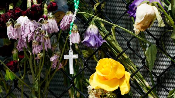 A cross hangs among wilting flowers at a makeshift memorial near the Champlain Towers South condo building.