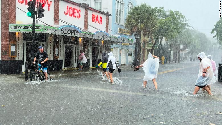 Determined visitors head to Sloppy Joe&#39;s bar while crossing a flooded Duval Street in Key West.