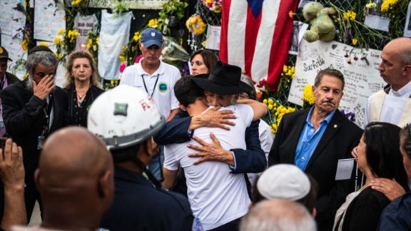 A member of Miami-Dade Fire Rescue hugs family members and friends of the victims at the "Surfside Wall of Hope & Memorial."