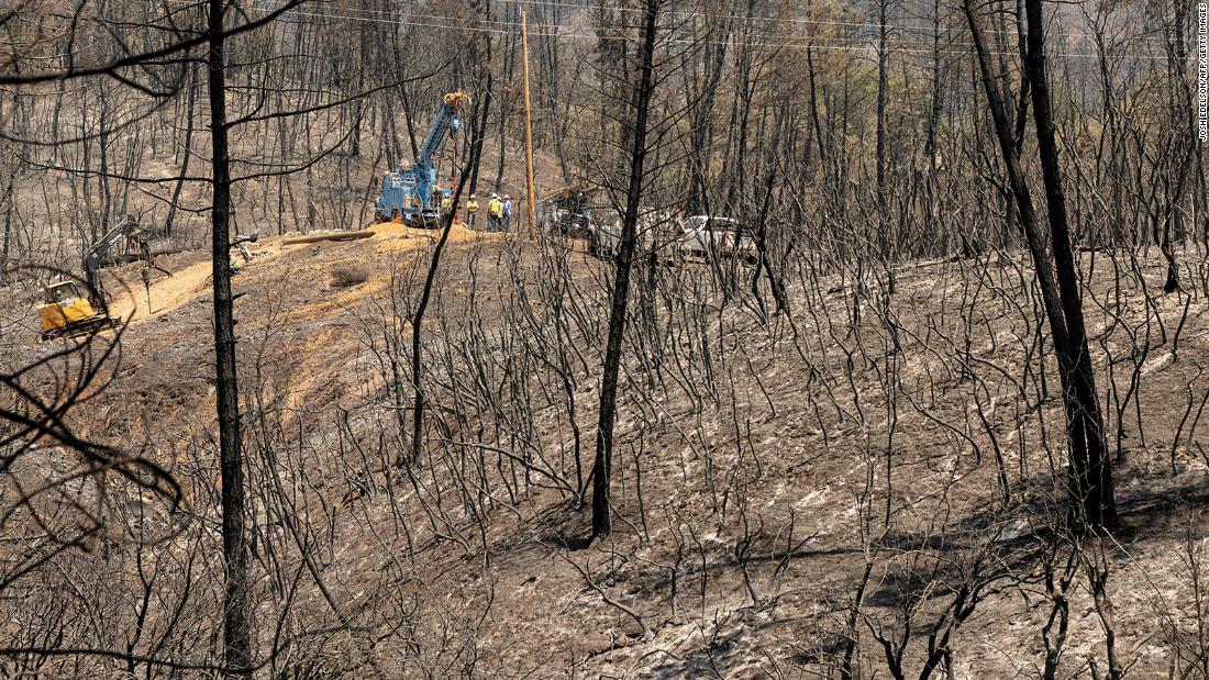 A utility crew works on power lines in front of a hillside that was burned by the Salt Fire in California&#39;s Shasta County.