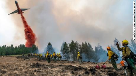 Wildland firefighters watch and take video with their cell phones as a plane drops fire retardant Monday on Harlow Ridge above the Lick Creek Fire, southwest of Asotin, Washington.