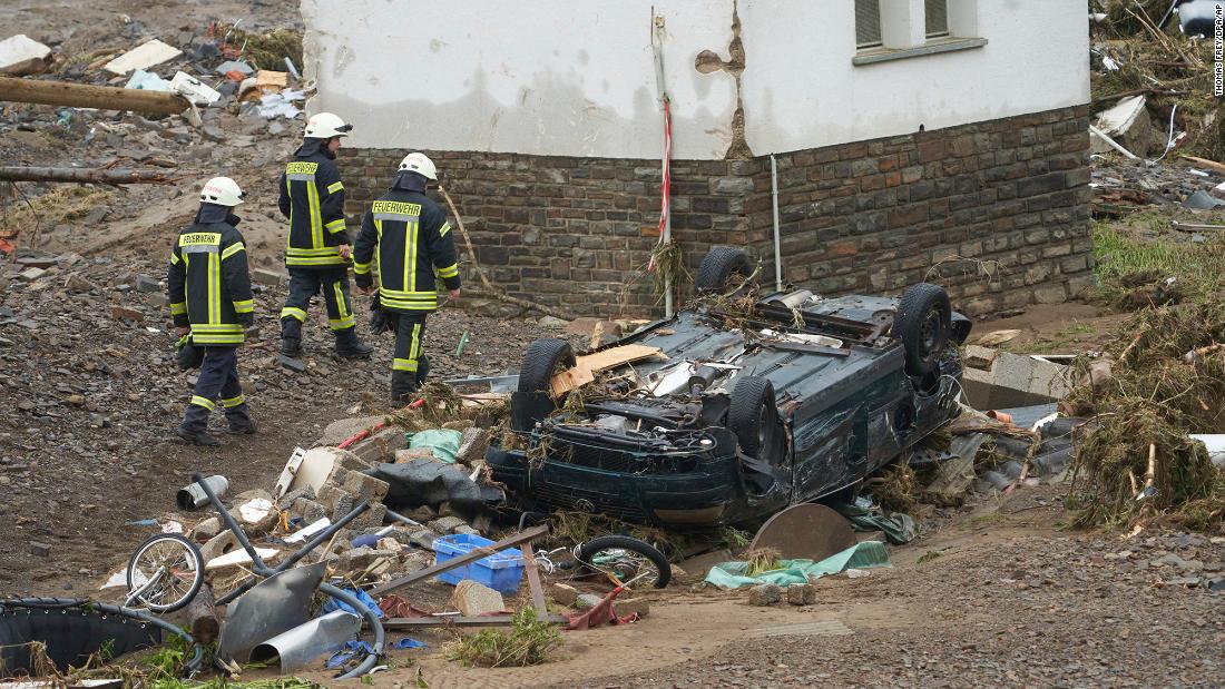 Firefighters walk past a car that was damaged by flooding in Schuld, Germany.