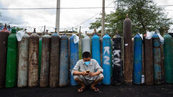 A man uses his mobile phone in front of empty oxygen canisters outside a factory in Mandalay on July 13.