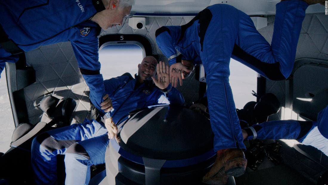 Mark and Jeff Bezos show &quot;Hi Mom&quot; written on their hands as the crew floats weightlessly in their capsule at the edge of space.