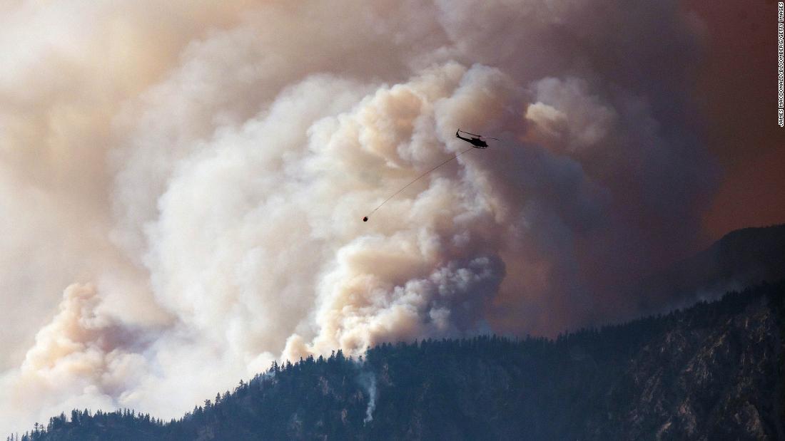 A helicopter prepares to make a water drop as smoke billows along the Fraser River Valley near Lytton, British Columbia, Canada, on Friday, July 2, 2021.