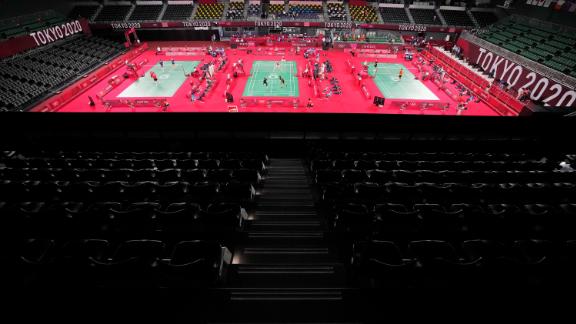 Badminton players compete amid rows of empty seats at Musashino Forest Sport Plaza.