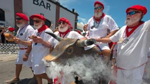 In this photo provided by the Florida Keys News Bureau, Ernest Hemingway look-alikes push a fake bull with smoke emanating from its nostrils during the &quot;Running of the Bulls&quot; Saturday, July 24, 2021, in Key West, Fla. A spoof of the event&#39;s namesake in Pamplona, Spain, the subtropical island city&#39;s version features fake bulls on wheels and is part of the annual Hemingway Days festival that honors author Ernest Hemingway, who lived and wrote in Key West throughout most of the 1930s. (Andy Newman/Florida Keys News Bureau via AP)