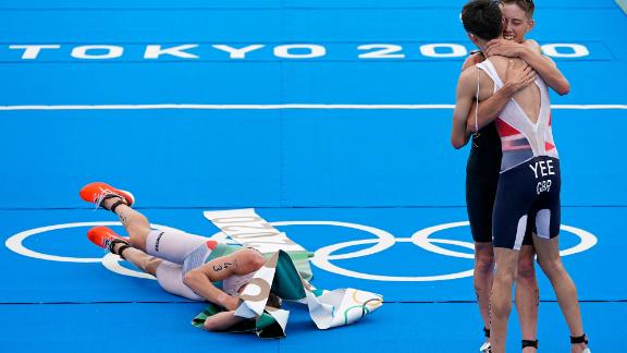 Norway's Kristian Blummenfelt lies on the ground wrapped in finish-line tape after he won the triathlon on July 26. On the right, silver medalist Alex Yee of Great Britain hugs bronze medalist Hayden Wilde of New Zealand.