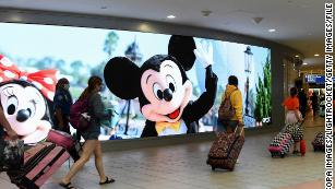 Travelers walk past a sign advertising Walt Disney World at Orlando International Airport as the July Fourth holiday weekend begins, on July 2, 2021.