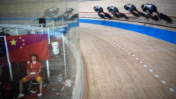 Cyclists from New Zealand competes in a team pursuit heat while China's Zhong Tianshi, left, takes a break on August 2.