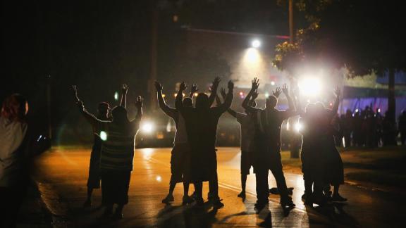 With their hands raised, residents gather at a police line as the neighborhood is locked down following skirmishes on August 11, 2014, in Ferguson, Missouri.