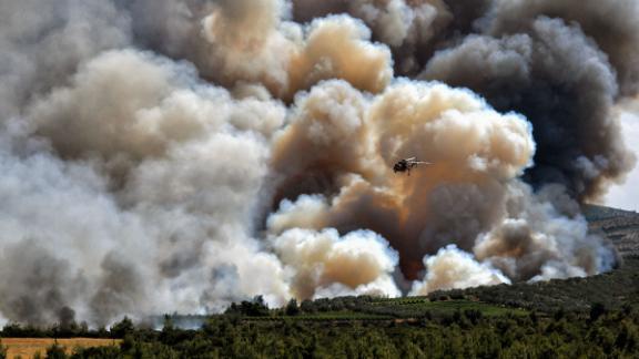 A firefighting helicopter passes in front of a cloud of smoke from a forest fire near Spathovouni village, southwest of Athens, Greece, on Friday, July 23.