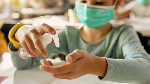 Close-up of elementary student disinfecting hands in the classroom due to COVID-19 pandemic. 