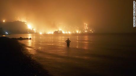 A man watches from the water as a wildfire approaches Kochyli beach near Limni village on Evia island.