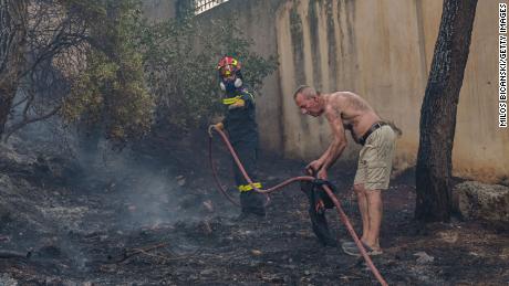  A local resident helps a firefighter battle a blaze before it spreads to houses in the Thrakomacedones area of northern Athens, Greece, on Saturday.