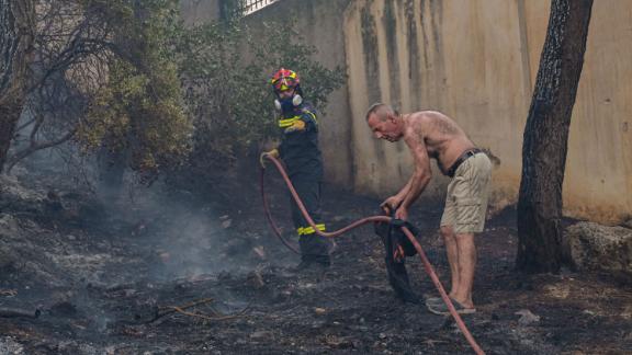 A resident helps a firefighter before fire spreads to houses in the Thrakomacedones area of Athens, Greece on August 7.