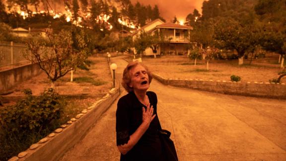 A resident reacts as a wildfire approaches her house in the village of Gouves, on the island of Evia, Greece.