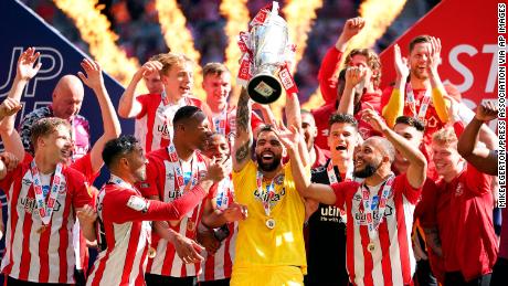 Brentford goalkeeper David Raya Martin lifts the trophy as they celebrate promotion to the Premier League after winning the Championship playoff final at Wembley Stadium.
